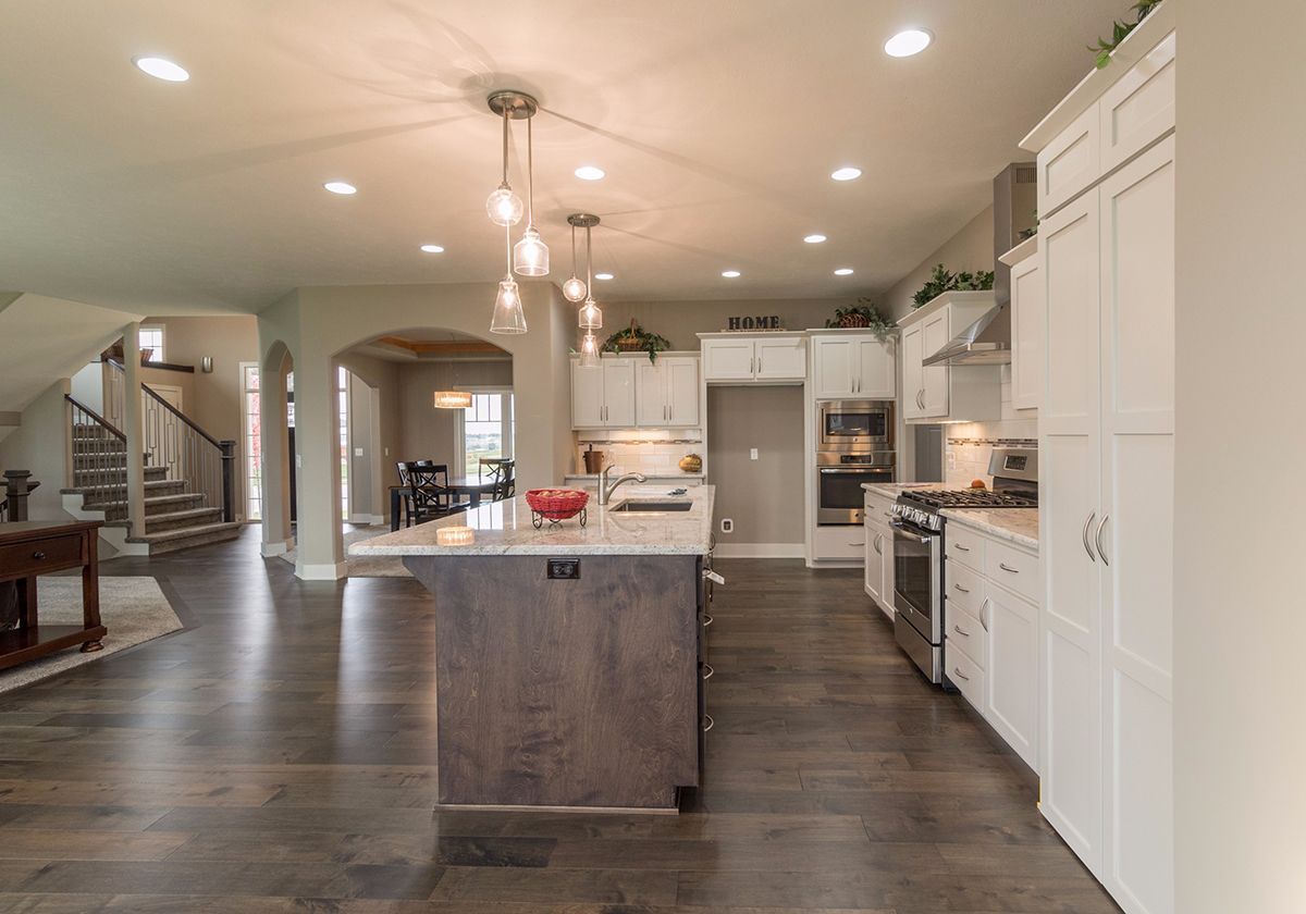 Bright open kitchen with white cabinets, dark wood floors, and a large island under recessed lights.