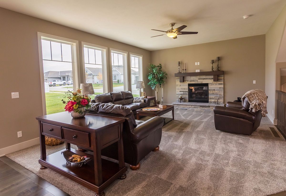 Spacious living room with beige walls, brown leather furniture, large windows, and a stone fireplace.