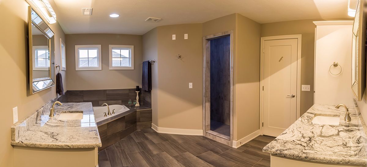 Modern bathroom with dual vanities, shower, toilet, and a living area visible through an open doorway.