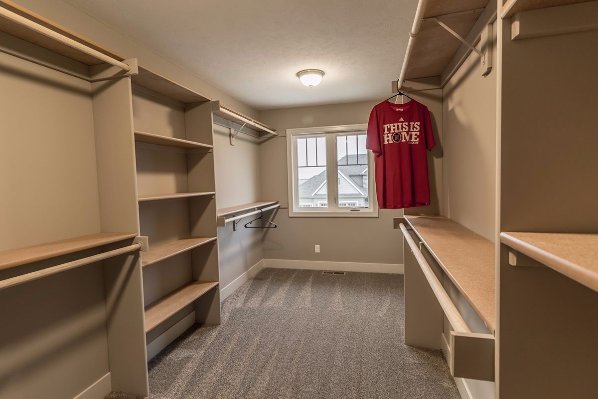 Walk-in closet with shelves, hanging rods, and a red jersey by a window.