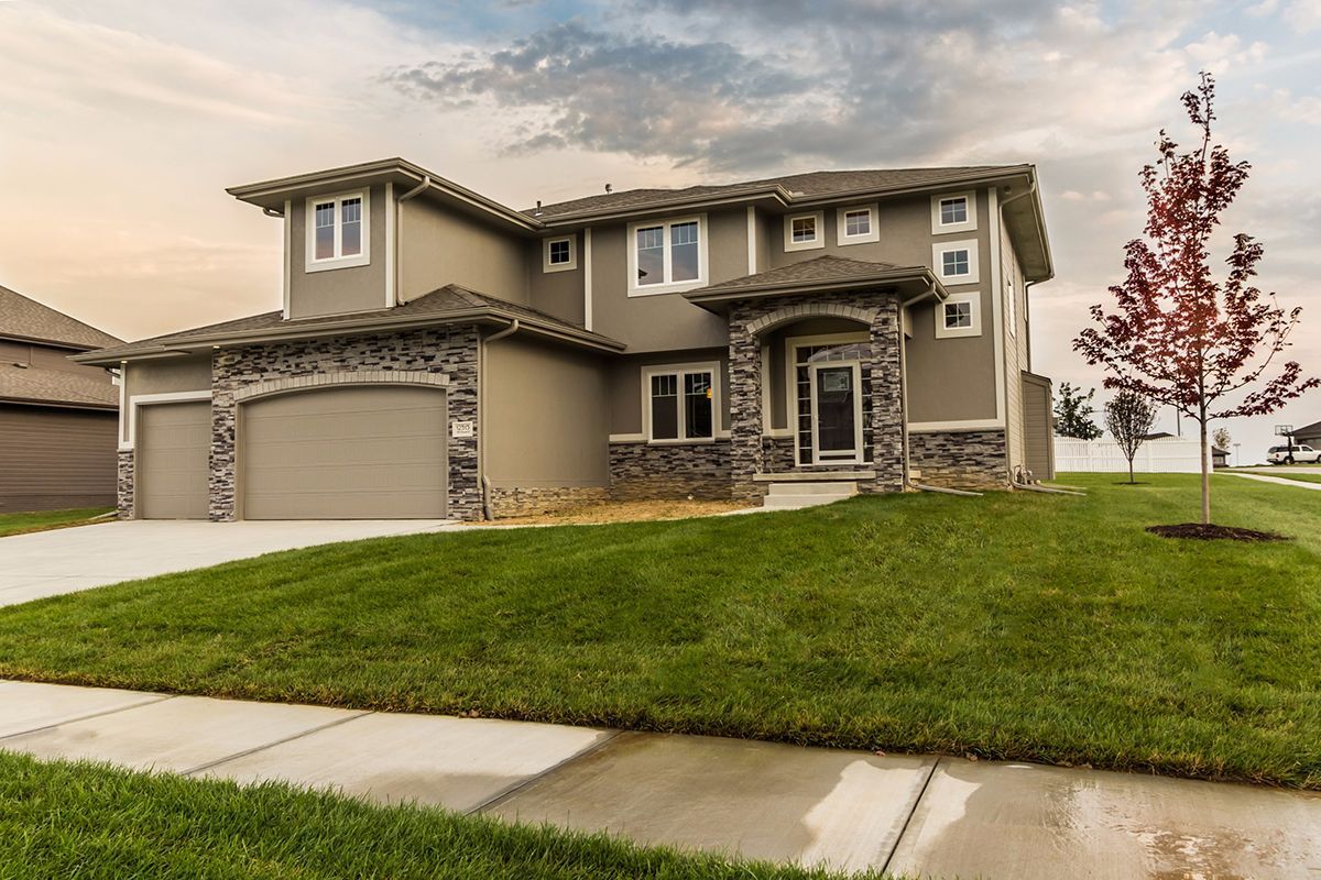 Two-story suburban house with beige exterior, stone accents, and a green lawn at dusk