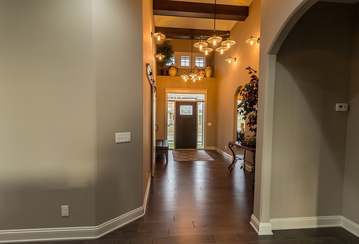 Empty hallway with dark wood floors, exposed beams, and a front door at the end.
