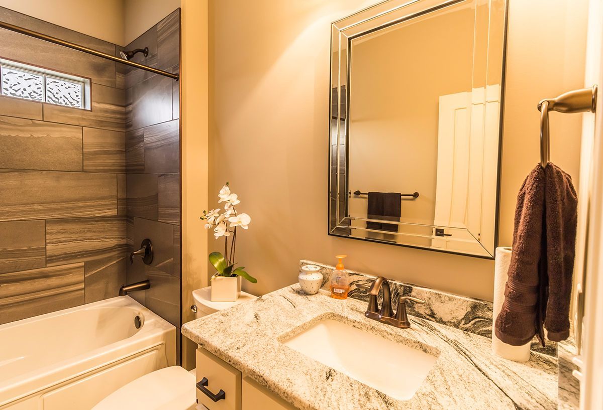 Modern beige bathroom with granite vanity, large mirror, bathtub, and towel rack