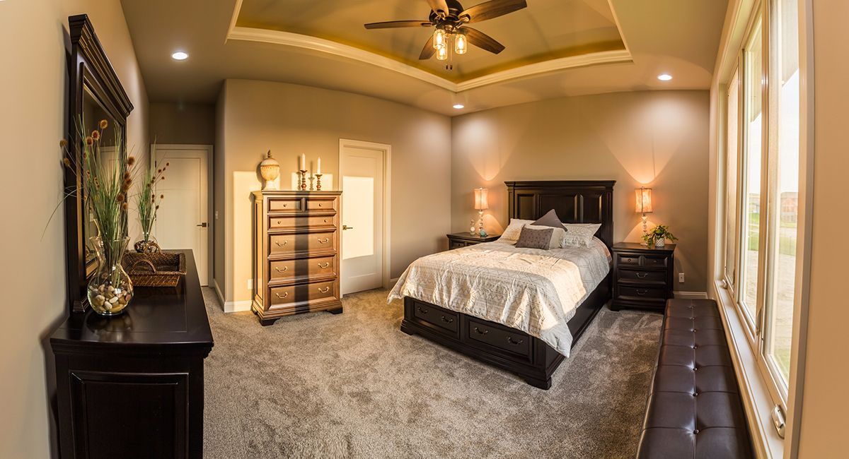 Spacious bedroom with a dark wood bed, patterned gray carpet, and large windows letting in warm light