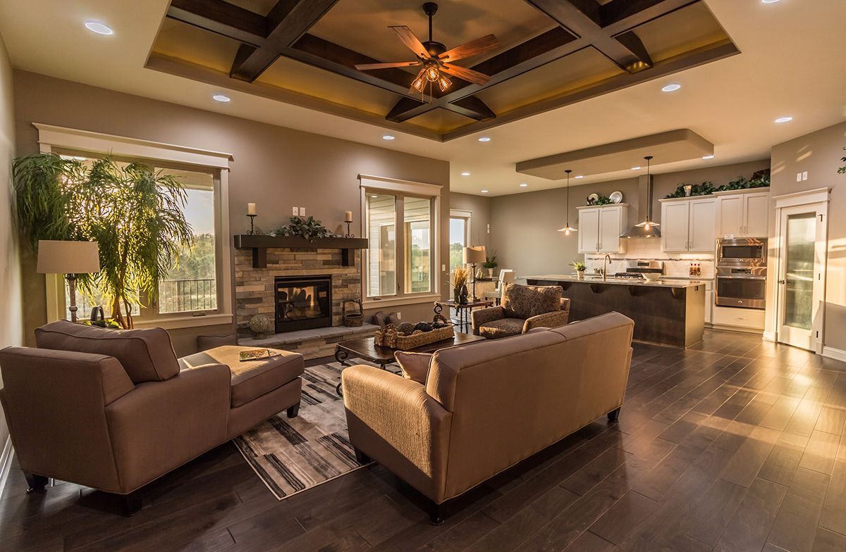 Spacious modern living room and kitchen with brown sofas, fireplace, ceiling fan, and warm lighting