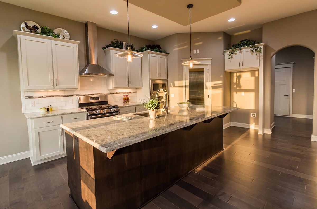 Modern kitchen with large island, granite counters, white cabinets, and warm recessed lighting