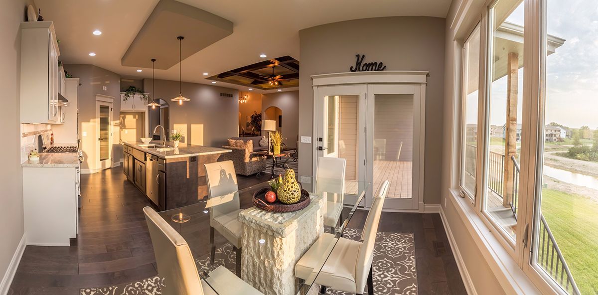 Modern open-concept kitchen and living area with island, dining table, and large windows overlooking a field