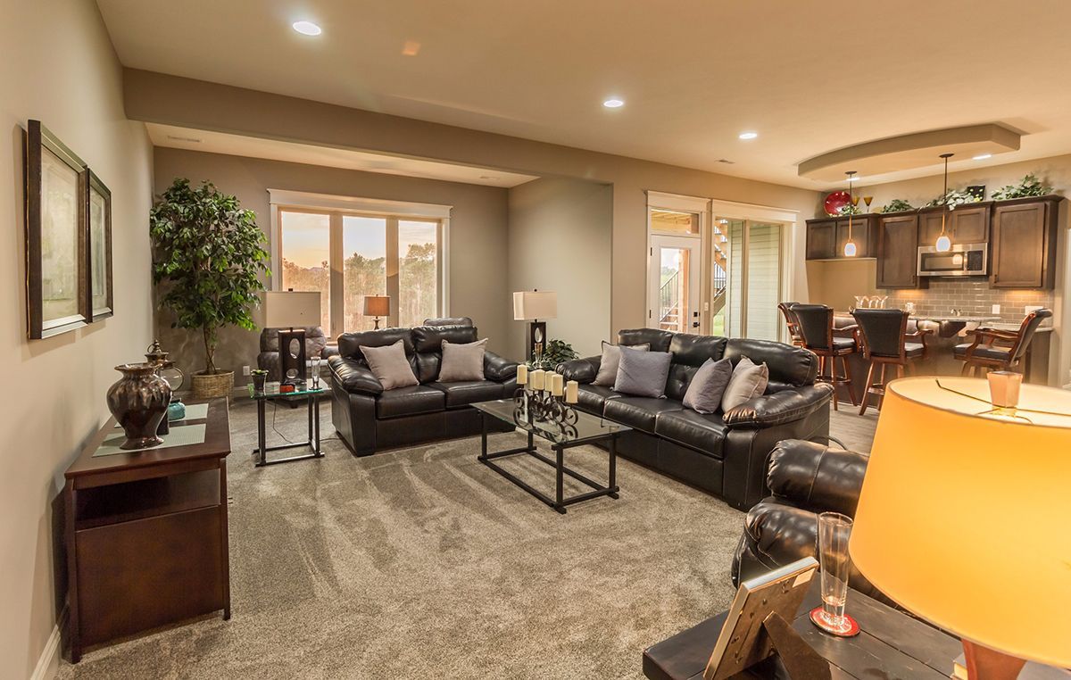Spacious beige living room with gray sectional sofa, coffee table, and kitchen visible in the background
