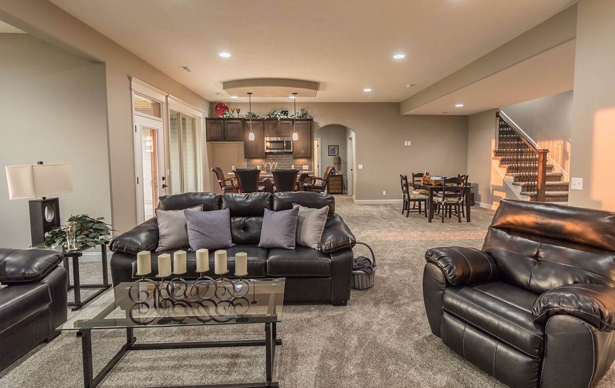 Spacious living room with leather sofas, gray rug, and open dining area under warm recessed lights