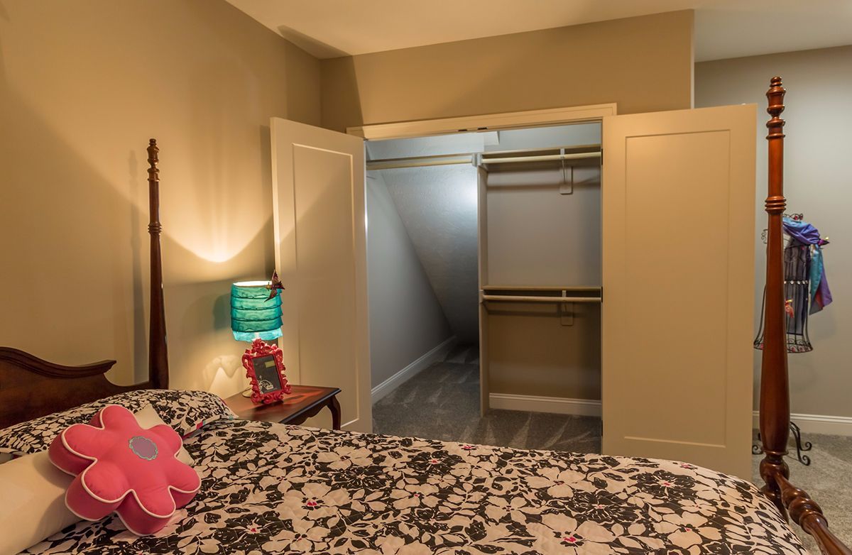 Bedroom with open closet doors, a bed with floral bedding, and a lit lamp beside the headboard.