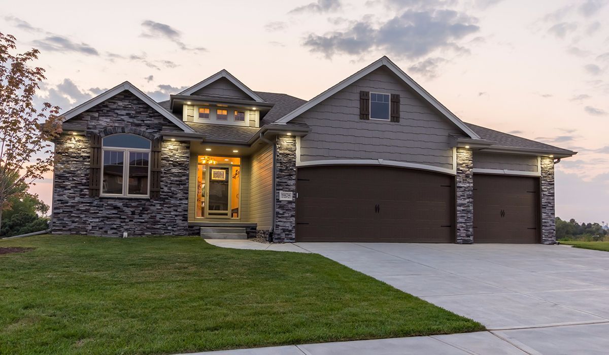 Suburban house at dusk with a lit front porch, stone accents, and a two-car garage.