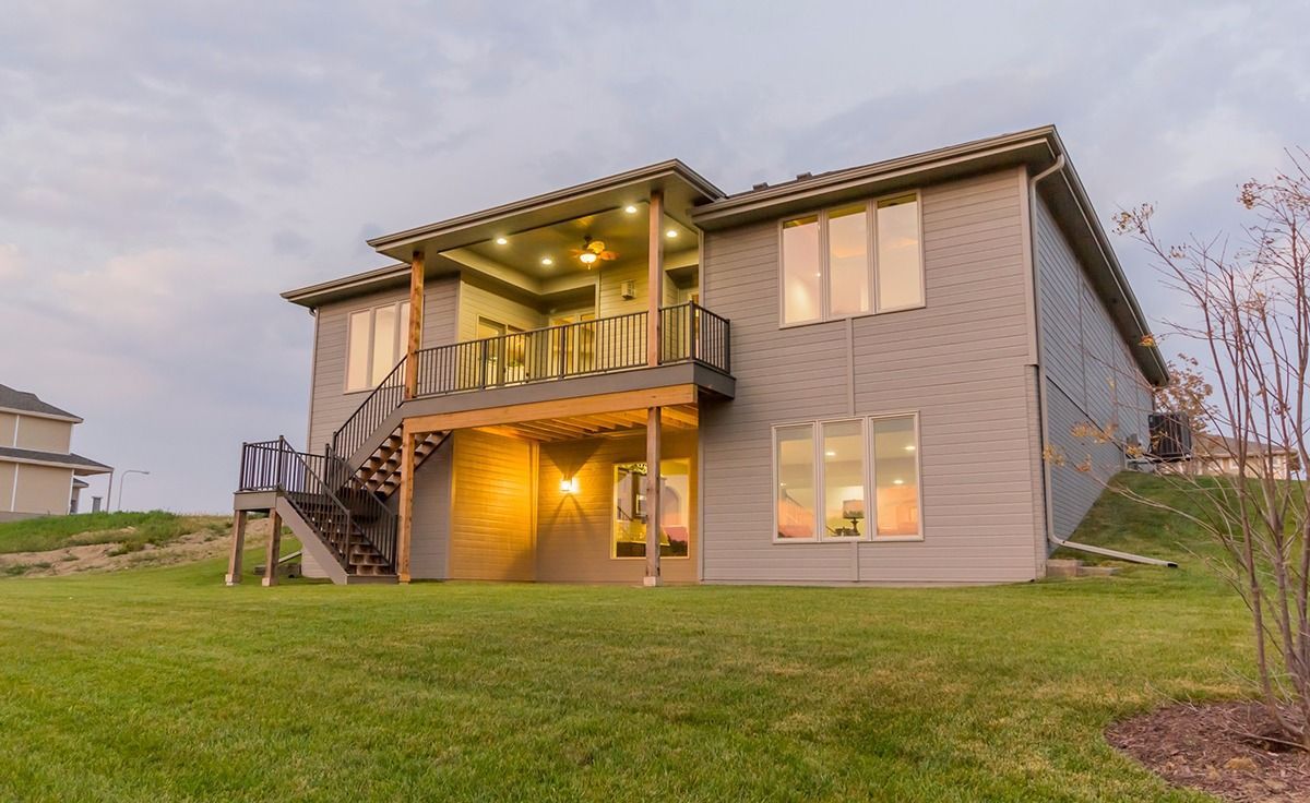 Two-story house with lit balcony and warm lights at dusk, set on a grassy lawn