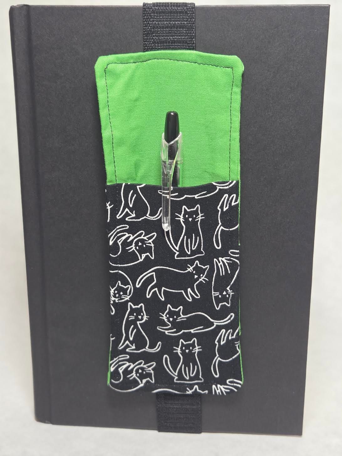 Small green-and-black fabric pocket with white animal prints clipped to a dark notebook cover