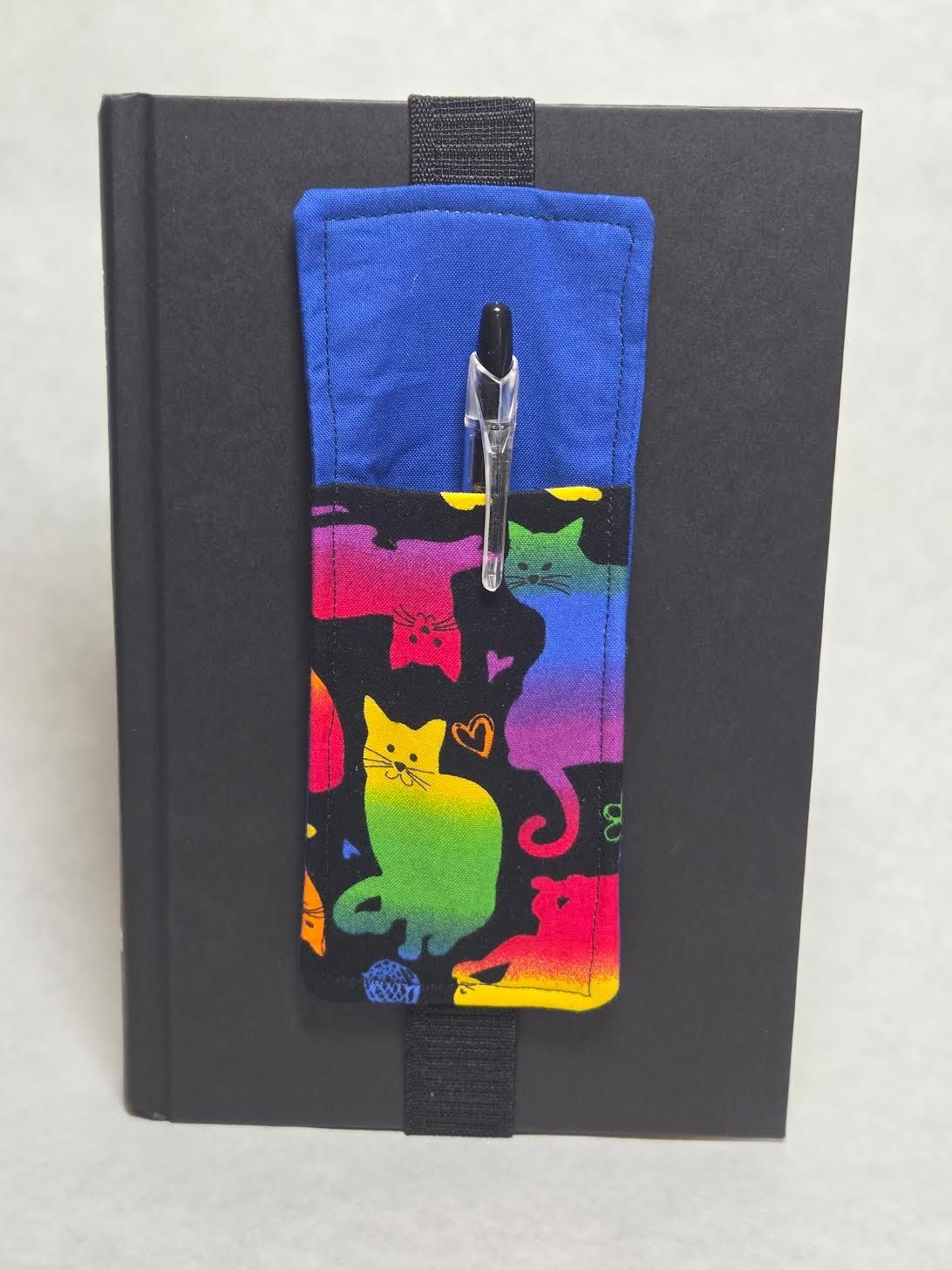 Black notebook with a blue cat-print pen holder and pen clipped on the front