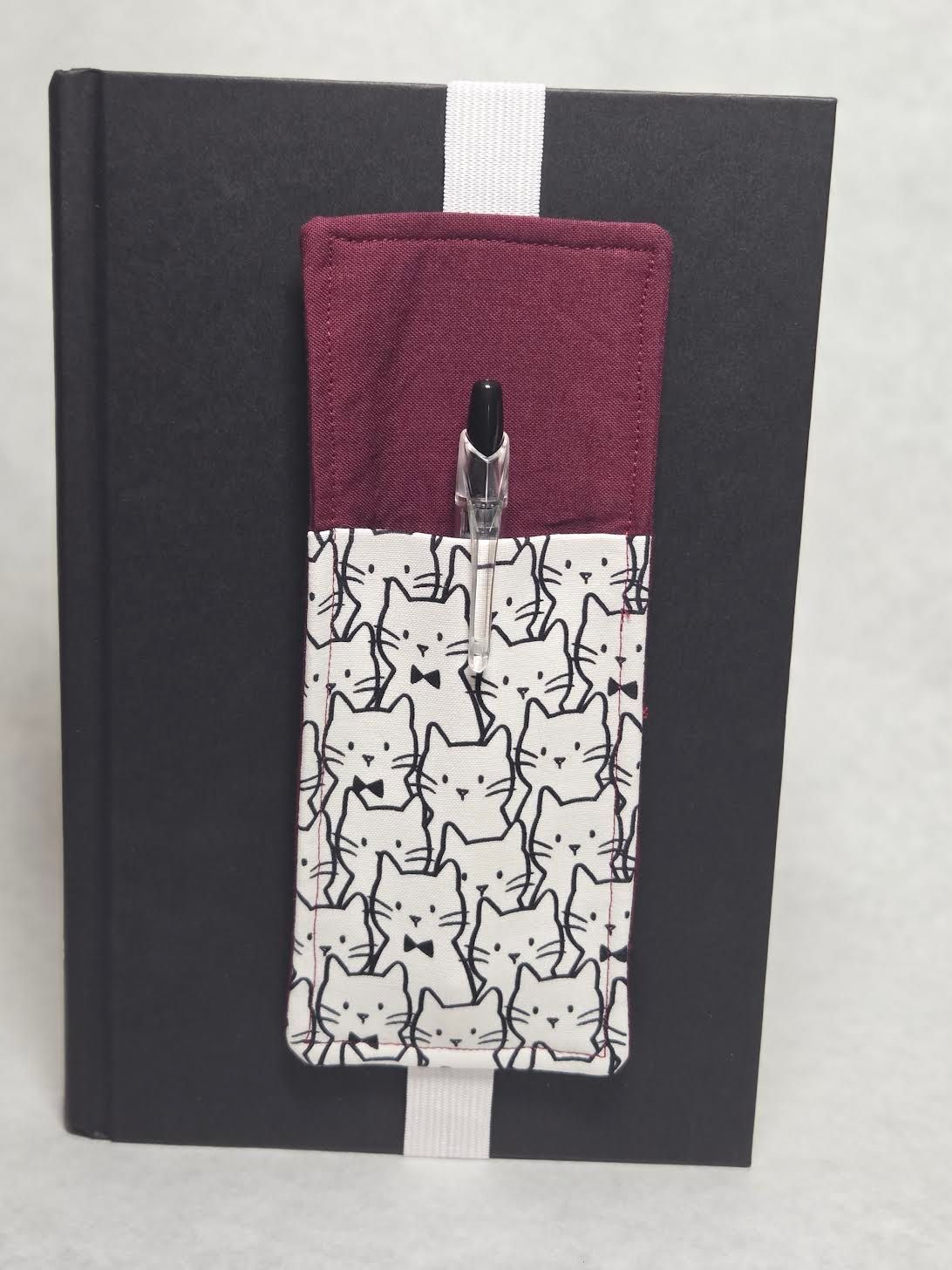 Black notebook with a white ribbon and maroon-and-cat patterned fabric bookmark on the cover