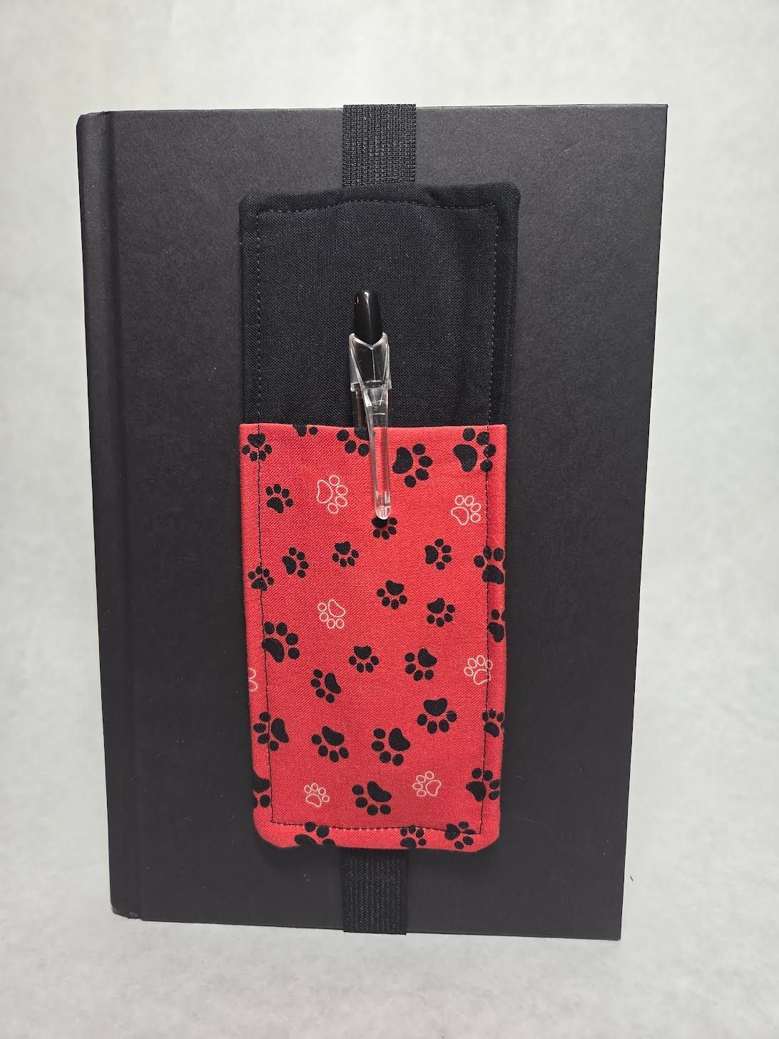 Black notebook with a red floral fabric pocket and black strap on the front.