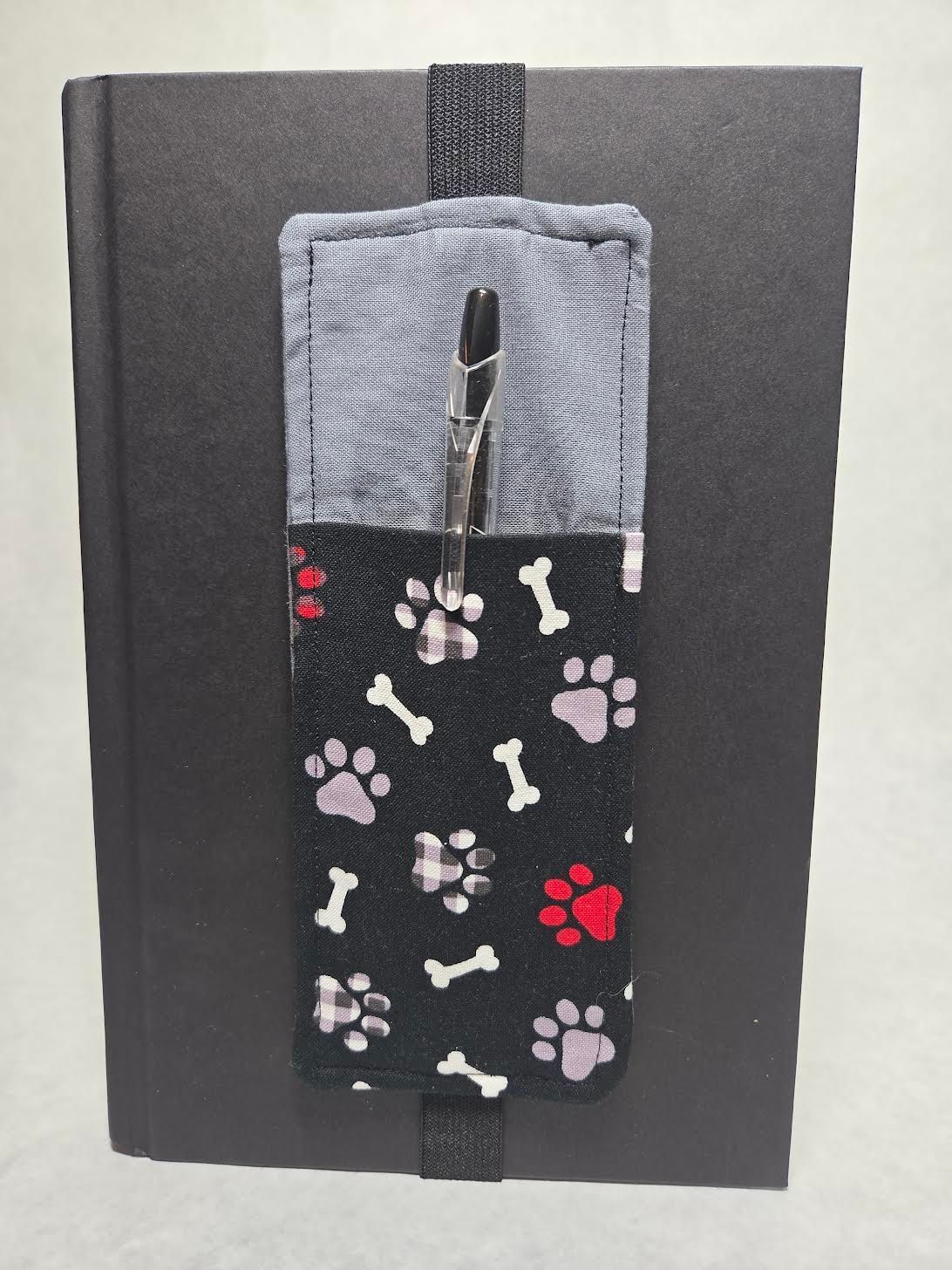Black notebook with a gray-and-black paw print fabric strap bookmark centered on the cover.