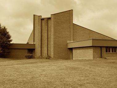 Brick building with geometric design and sloped roof against a cloudy sky.