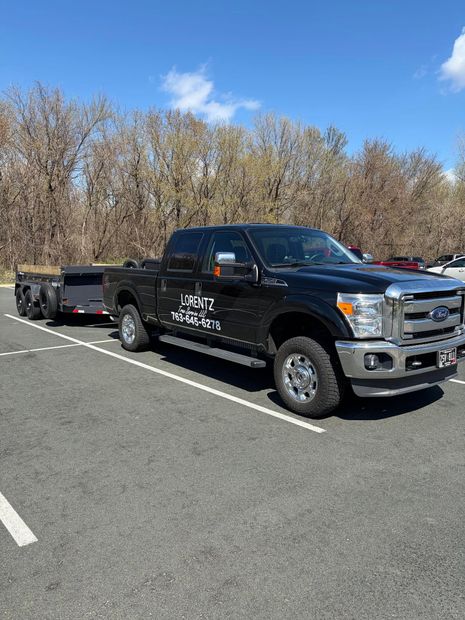 Black pickup truck with trailer parked in a lot on a sunny day, trees in the background
