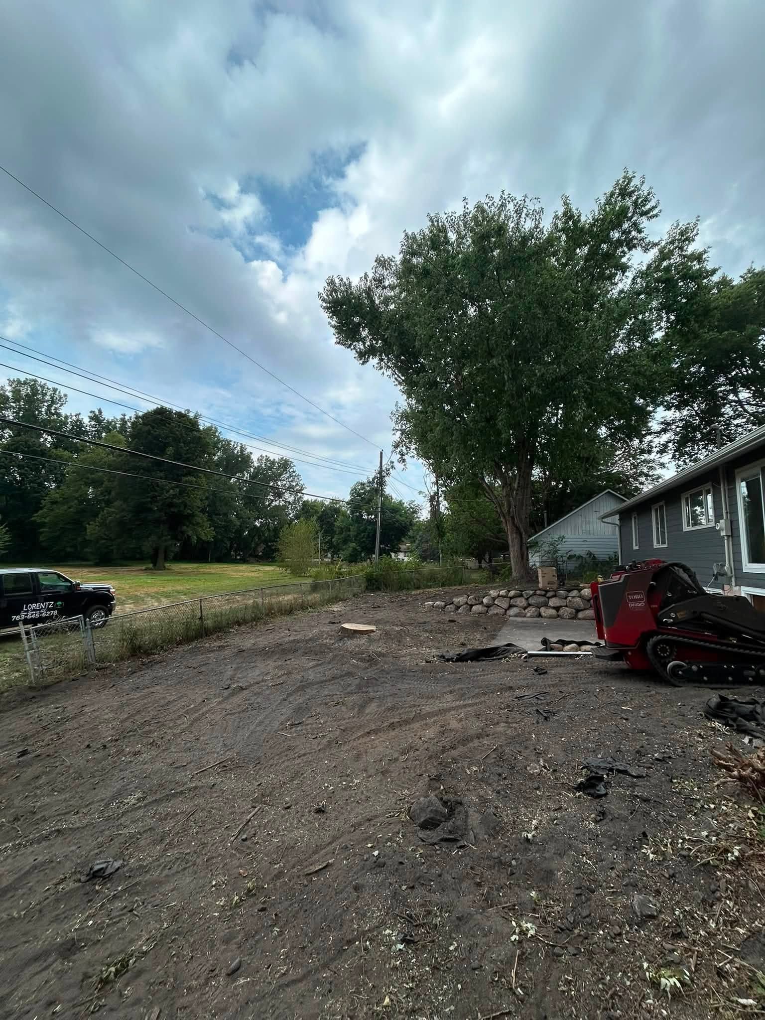 Gravel driveway beside a house with a red mower and trees under a cloudy sky.