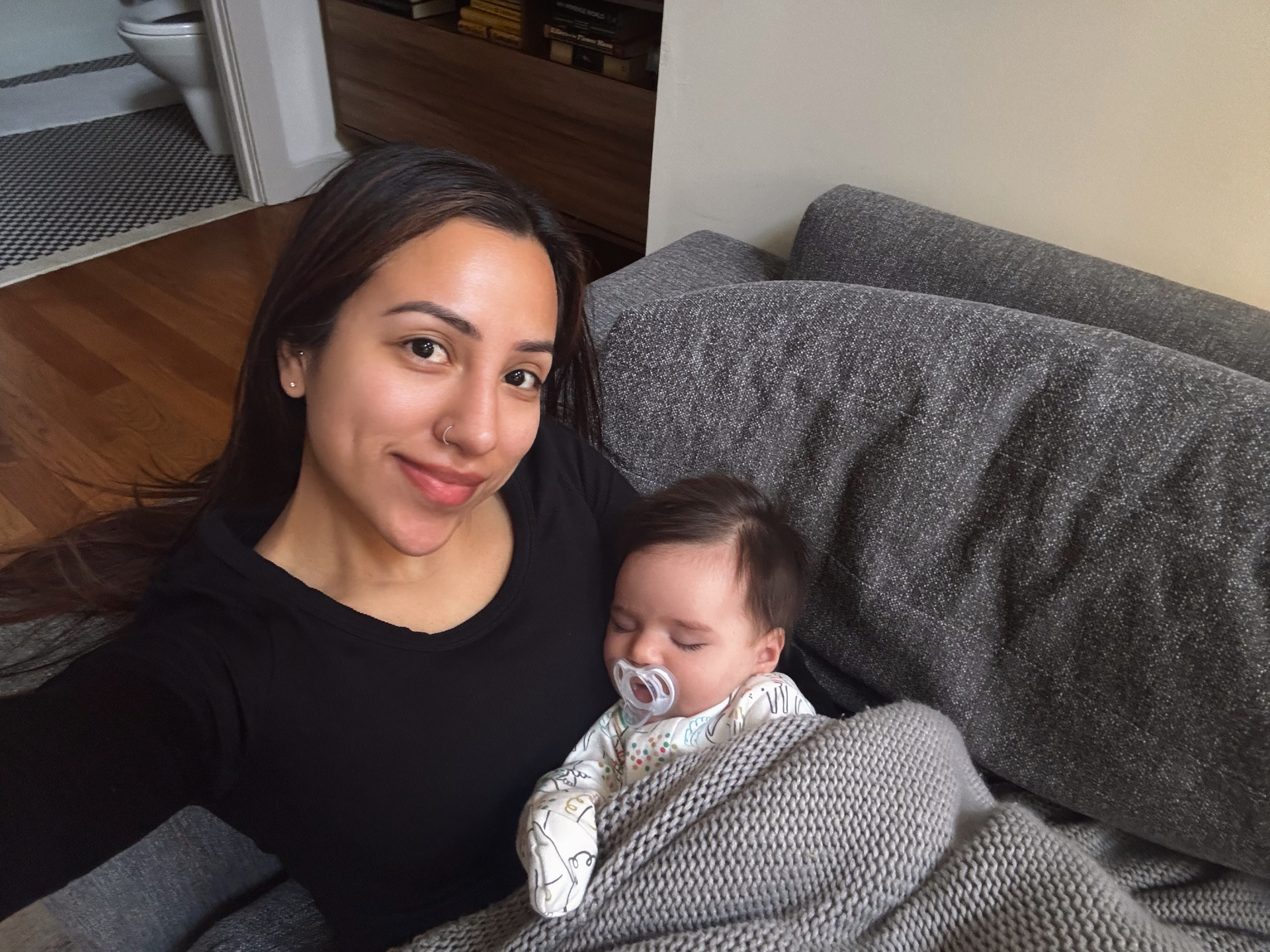 Woman holding a smiling baby wrapped in a gray blanket on a couch