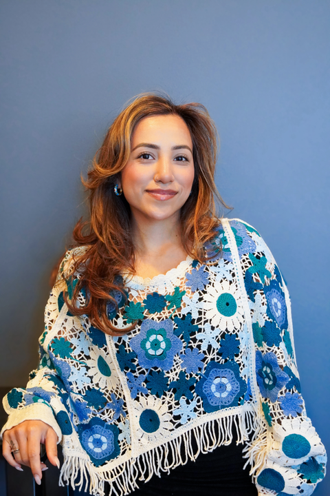 Woman seated against a blue background, wearing a blue floral top and smiling softly.