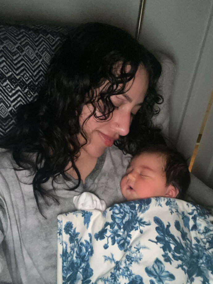 Woman cuddling a baby under a blue floral blanket on a couch