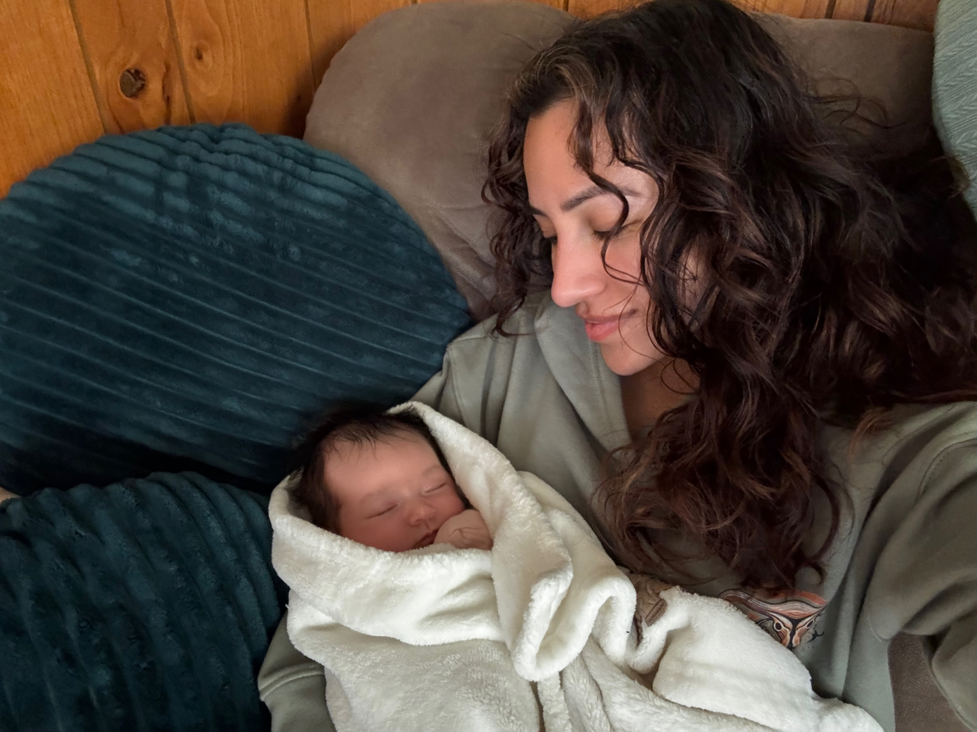 Woman holding a sleeping baby wrapped in a white blanket on a couch