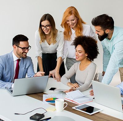 Group of people around a table looking at a laptop and documents, smiling and collaborating.