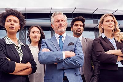 Group of business professionals standing confidently with arms crossed in front of a modern building.