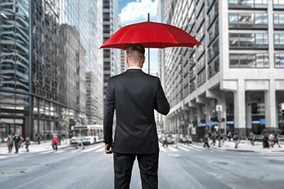 Man in suit holding a red umbrella in a city street.