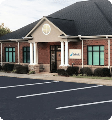 Brick building with black roof, white columns, and Priority logo sign.