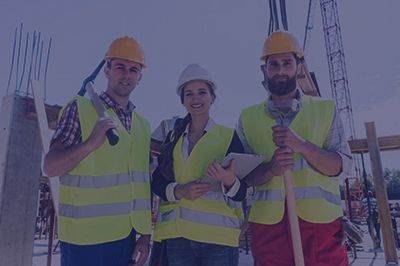 Construction workers wearing safety vests and hard hats at a construction site, smiling.