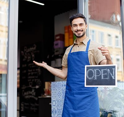 Man in blue apron stands in doorway, holding 