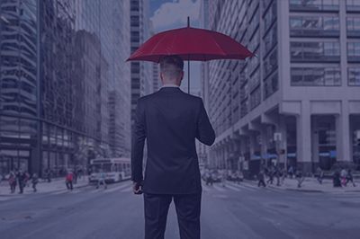 Man in a suit holds a red umbrella in a city street, shielding himself from above.