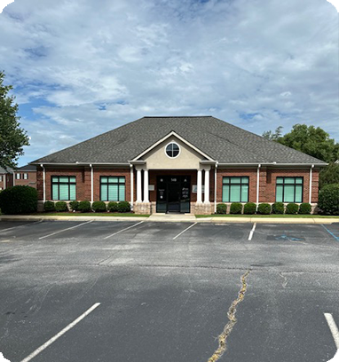 Brick building with white columns, arched window, and empty parking lot.