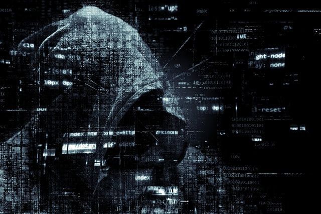 A person in a hoodie is standing in front of a computer screen.