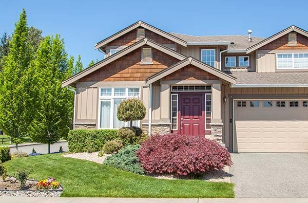 Two-story house with tan siding, red front door, and manicured landscaping under a blue sky.
