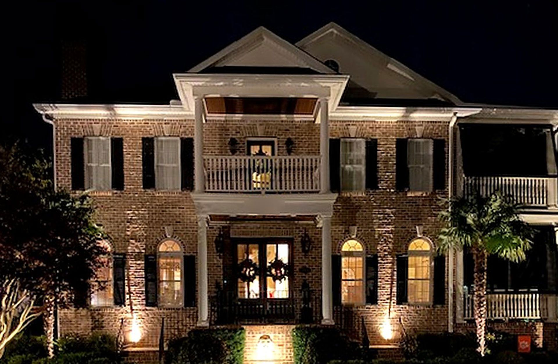 Lit brick two-story house at night, warmly lit with lights on the porch and windows.
