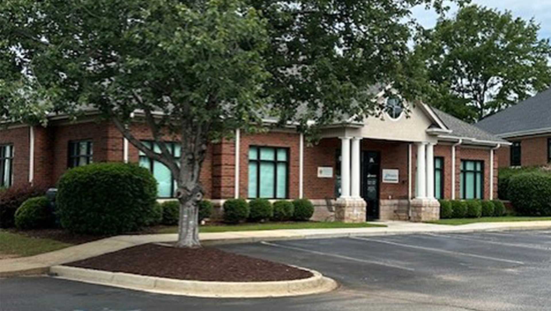 Brick office building with white columns, green awnings, and a tree-lined parking lot