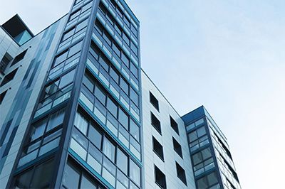 Modern multi-story building with glass windows, blue and white facade against a pale blue sky.