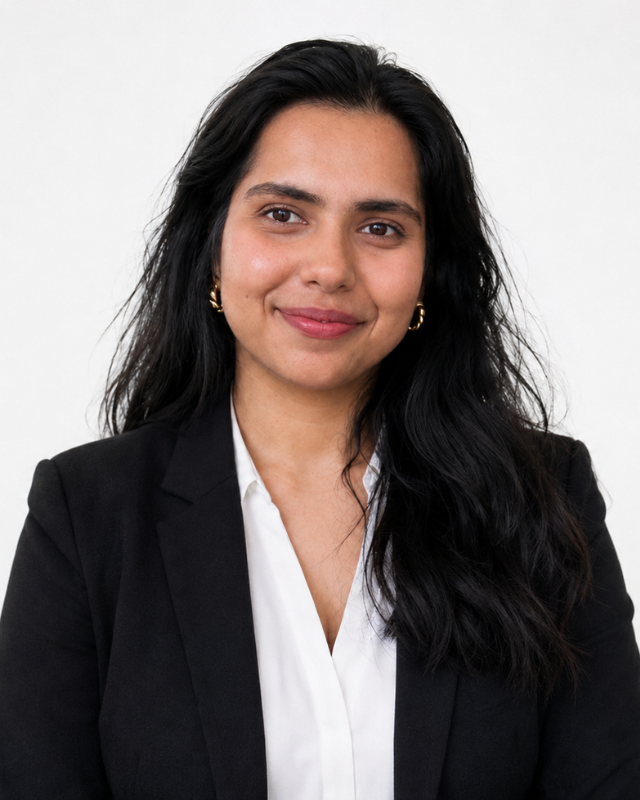 A headshot of a woman smiling with long black hair against a white background, and wearing a black blazer and a white blouse