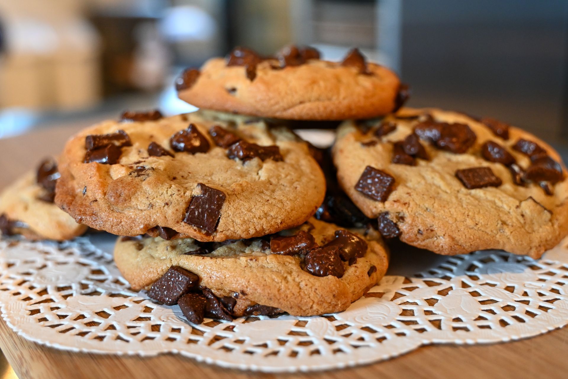 A stack of chocolate chip cookies on a lace napkin on a table.