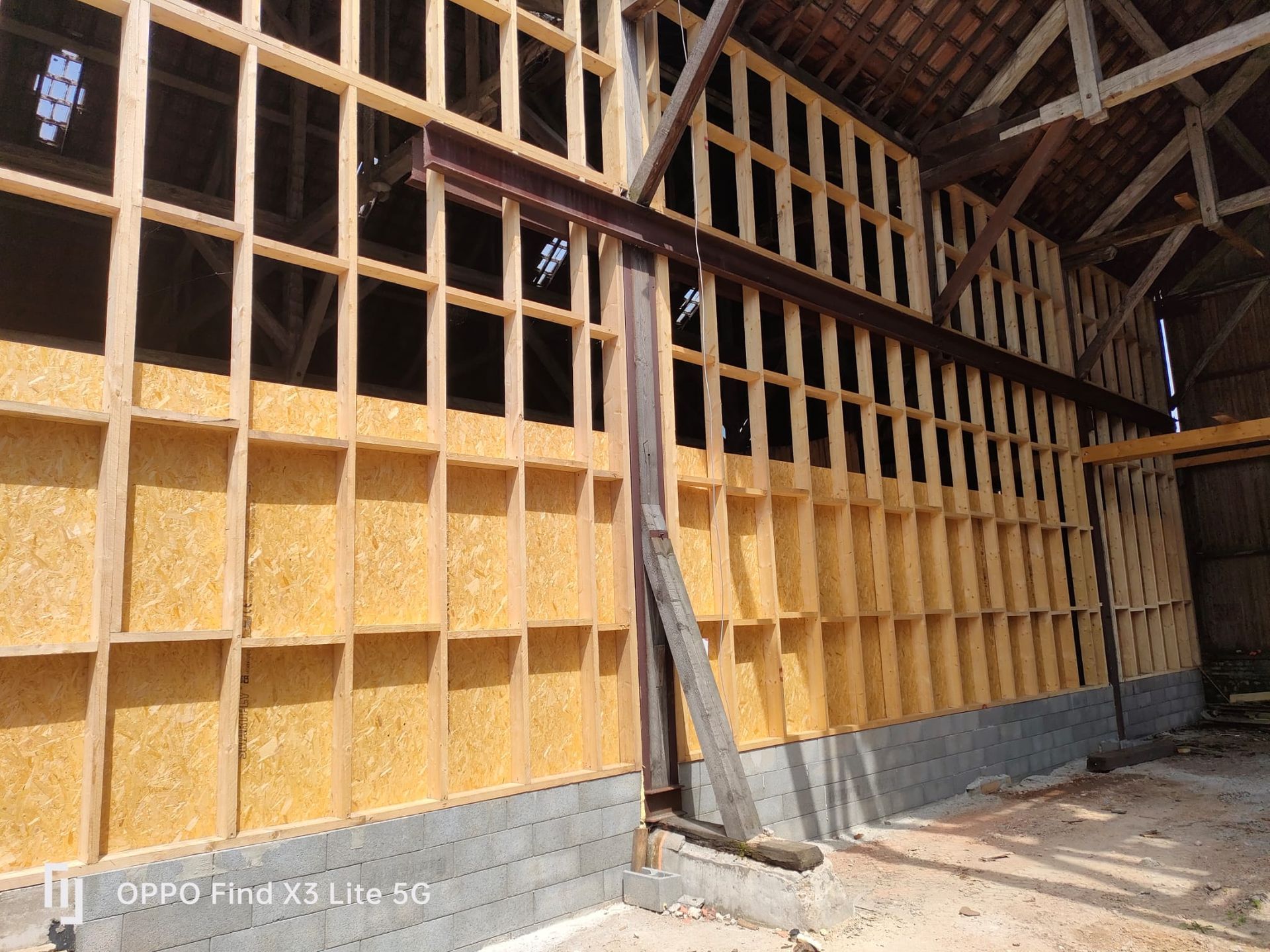 Intérieur d'une grange en construction, avec charpente en bois, isolation et poutre en acier.