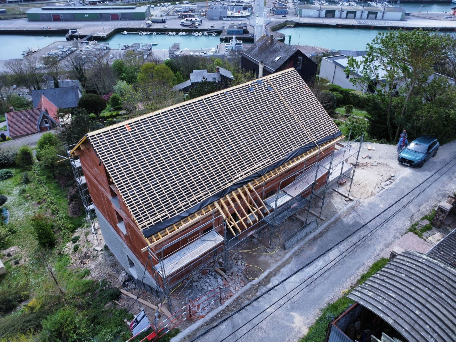 Bâtiment en construction avec un toit de tuiles presque terminé, donnant sur un port.