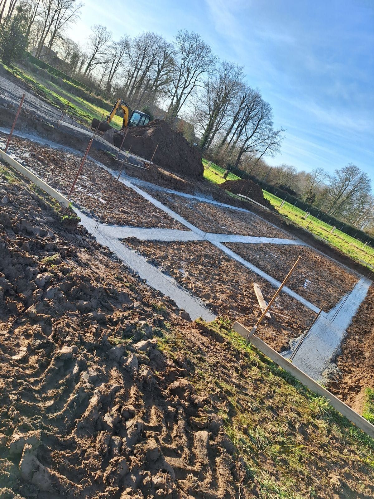 Chantier de construction avec ossature de fondation, excavatrice en arrière-plan, par une journée ensoleillée.
