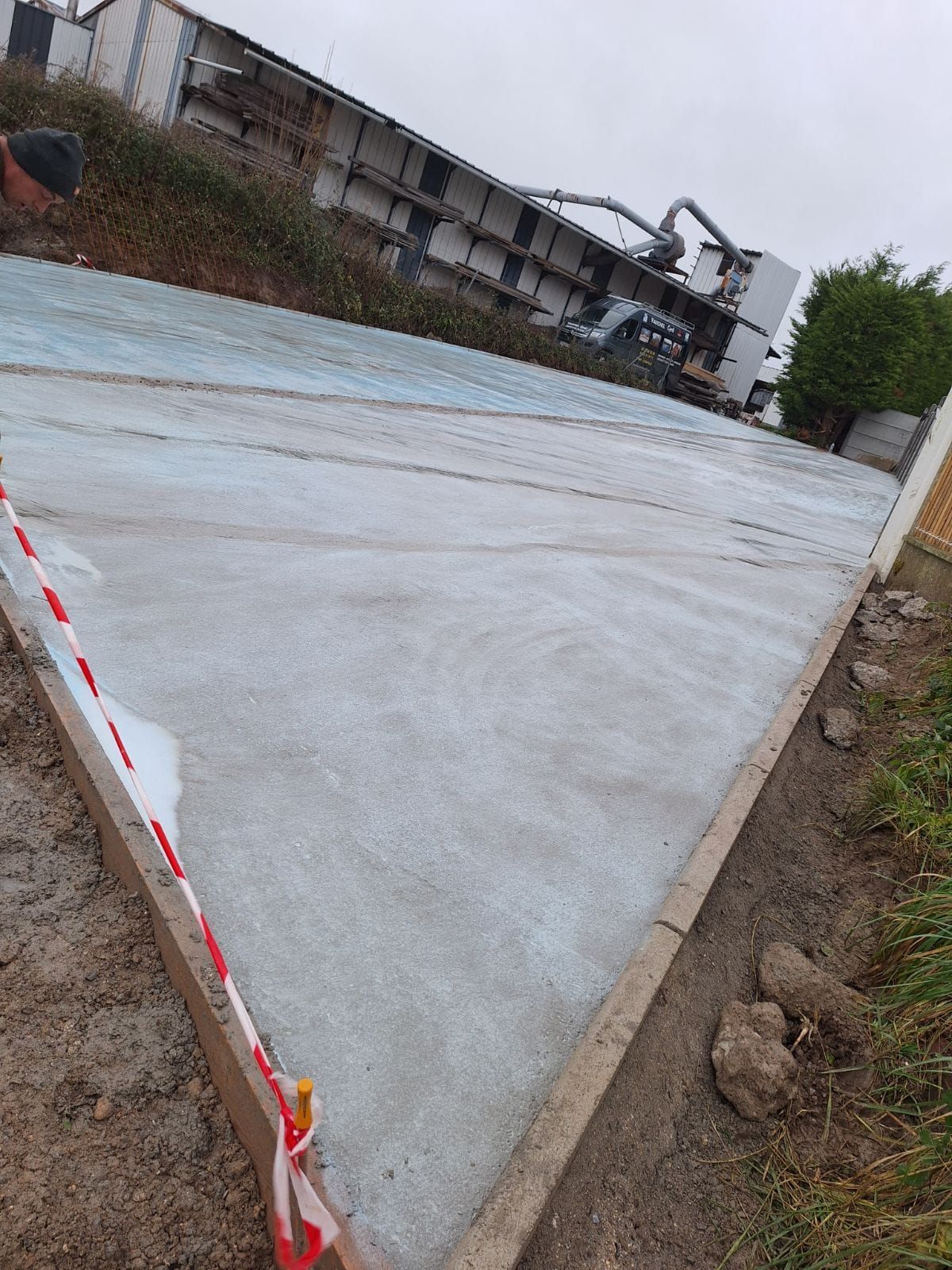 Chemin en béton fraîchement coulé, balisé par du ruban de signalisation, menant à un bâtiment en construction.
