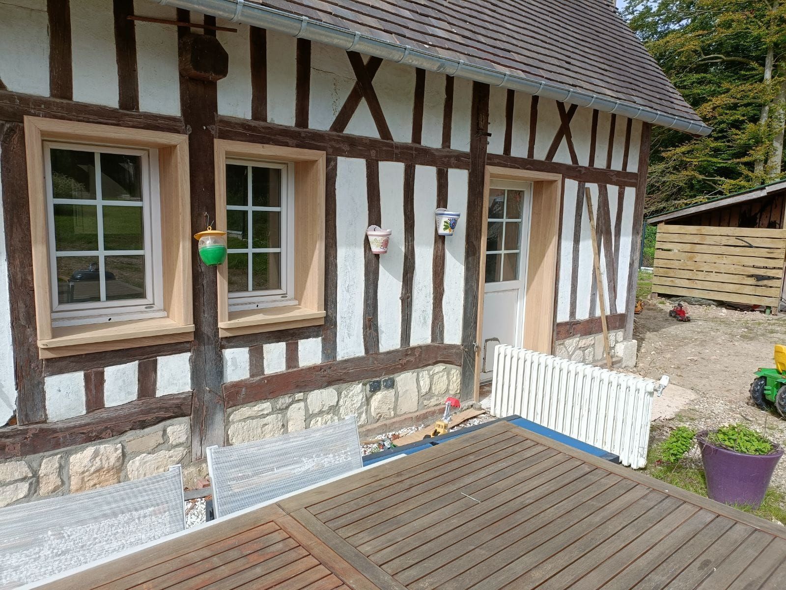 Maison à colombages avec une table en bois, deux fenêtres et une porte donnant sur un patio.