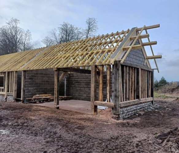 Structure en bois en construction, charpente apparente, chevrons apparents, extérieur patiné, aménagement extérieur.