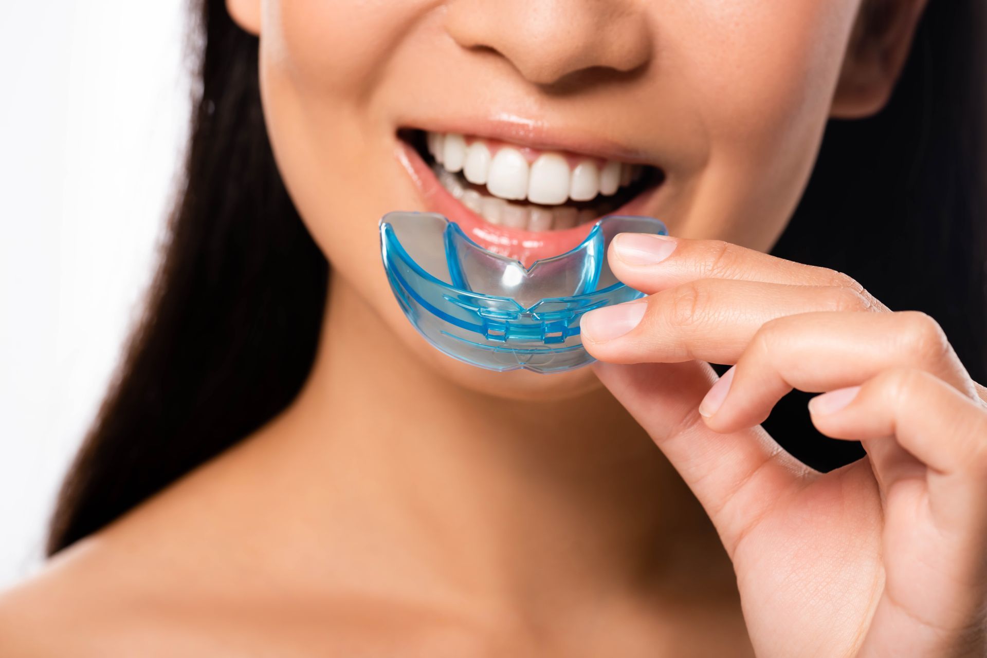 A person holds a blue, clear dental aligner or orthodontic tray up to their mouth.